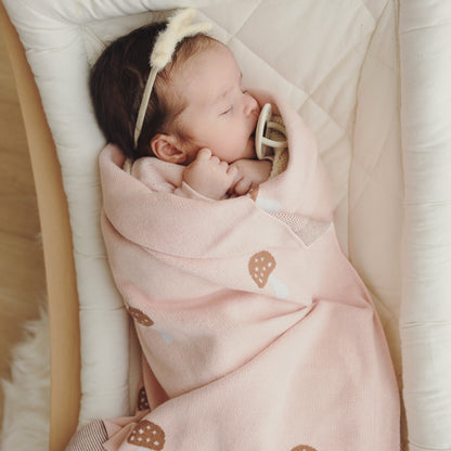 Newborn baby sleeping in a crib with a pink swaddle blanket with mushroom pattern