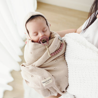 Newborn baby wrapped in a beige swaddle with a pacifier, held by a person.