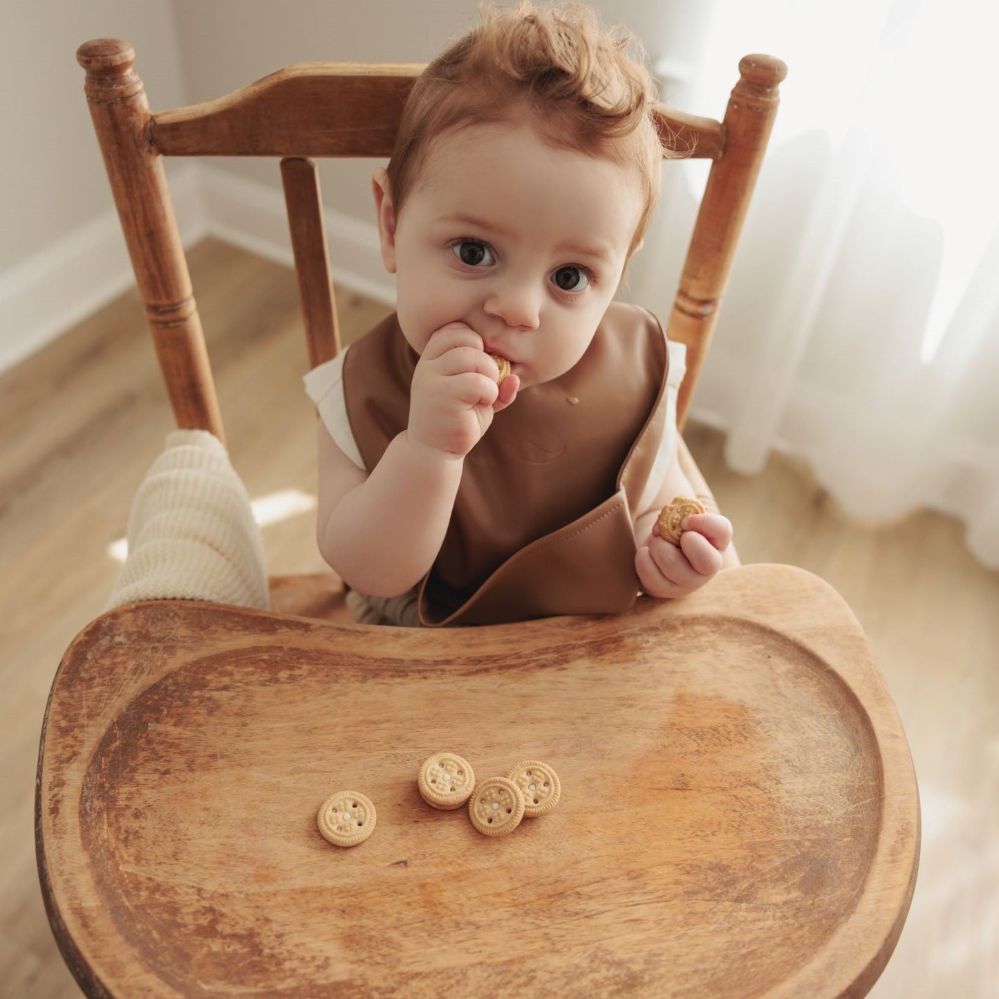 Baby sitting on a wooden chair with a wooden tray holding cookies wearing classic vegan leather easy clean bib 