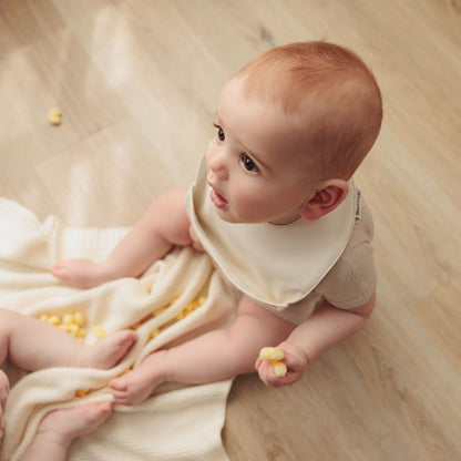 Baby sitting on a wooden floor with a white blanket wearing a soft vegan leather easy clean baby bibs with adjustable snaps