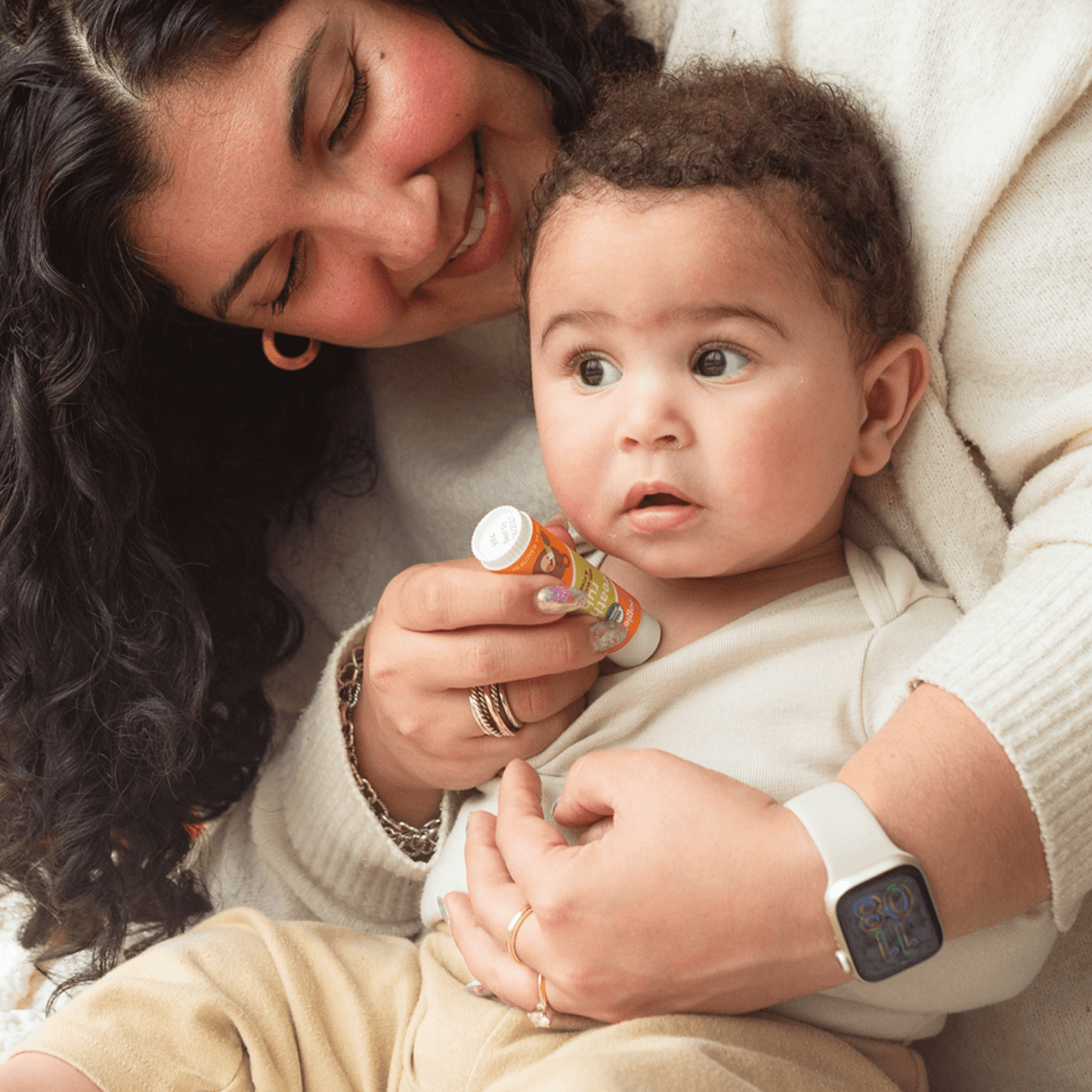 A woman holding a baby and using oogiebear Breathing Rub organic baby balm tube with eucalyptus and rosemary for congestiont on the babys chest. 