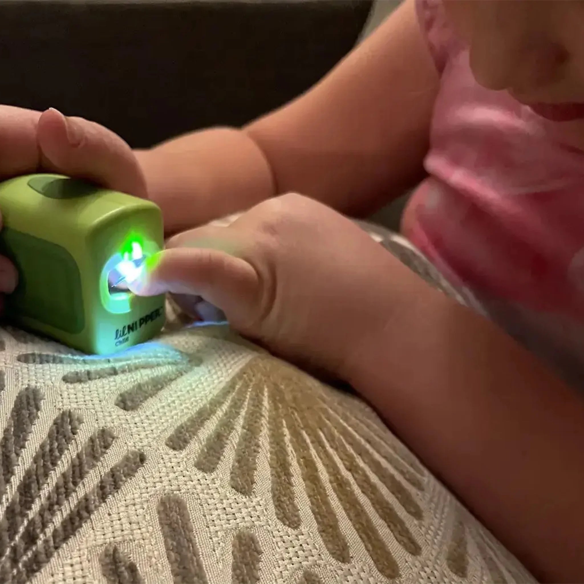 Close-up of child hands using green Lil Nipper electric nail clipper for fingernail trimming. Bright light shining over the safety nail slot.