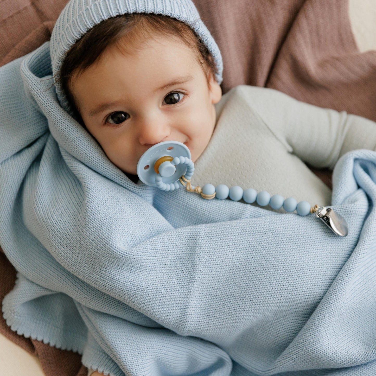 Baby wrapped in a light blue blanket with a pacifier, wearing a matching hat.
