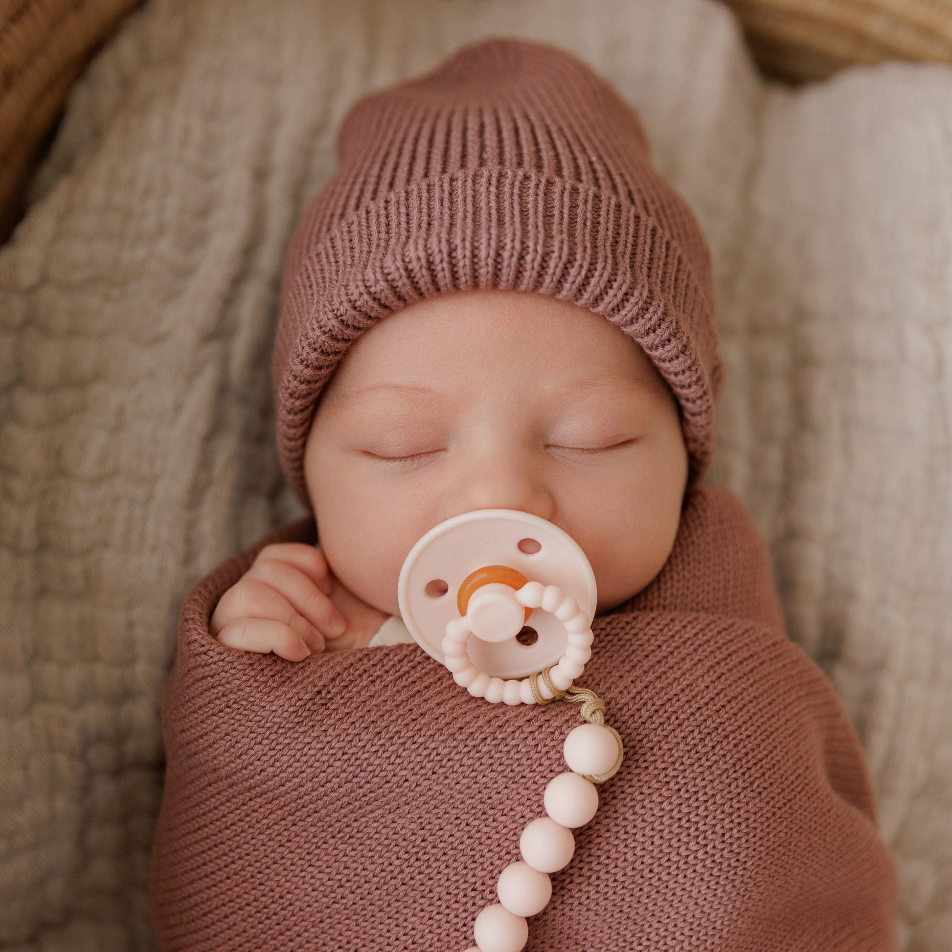 Newborn baby sleeping peacefully with a pink knit hat and a Luladream pacifier 