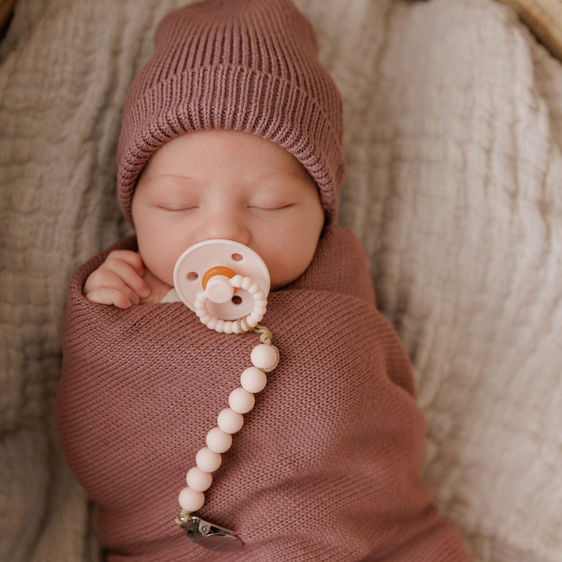 Newborn baby wrapped in pink blanket and wearing pink knit hat with a Luladream Pacifier pacifier