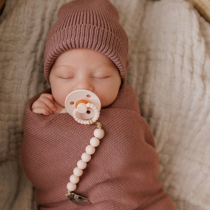 Newborn baby wrapped in pink blanket and wearing pink knit hat with a Luladream Pacifier pacifier
