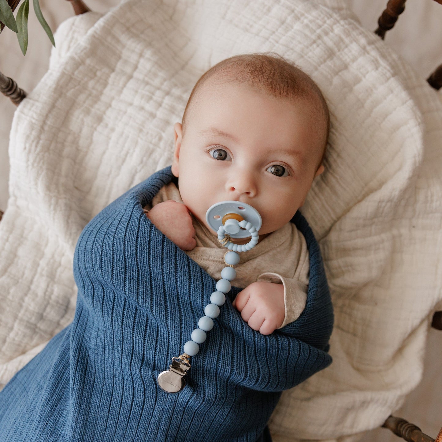 Baby wrapped in a blue blanket with a Luladream premium pacifier. 