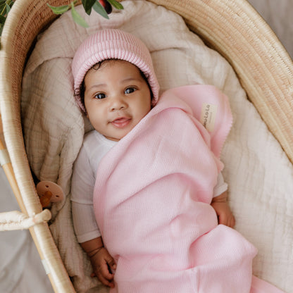 Baby wrapped in a pink blanket, bleu-la-la, and wearing a pink hat in a crib.