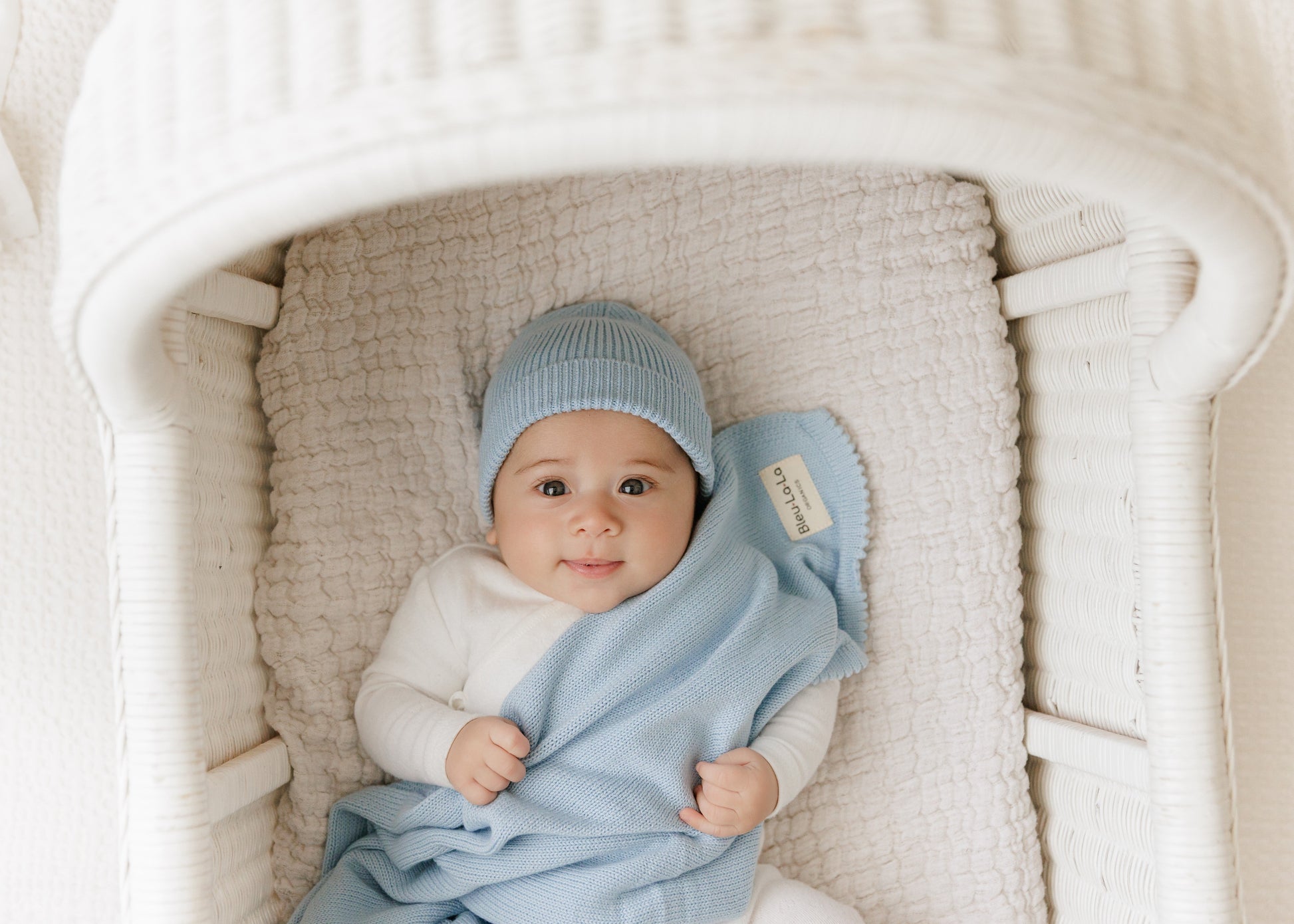 Baby wrapped in a blue blanket and wearing a matching hat in a white crib.
