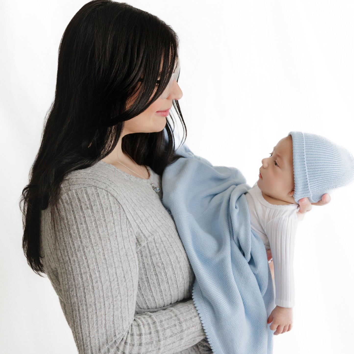 Woman holding a baby wrapped in a light blue blanket against a white background