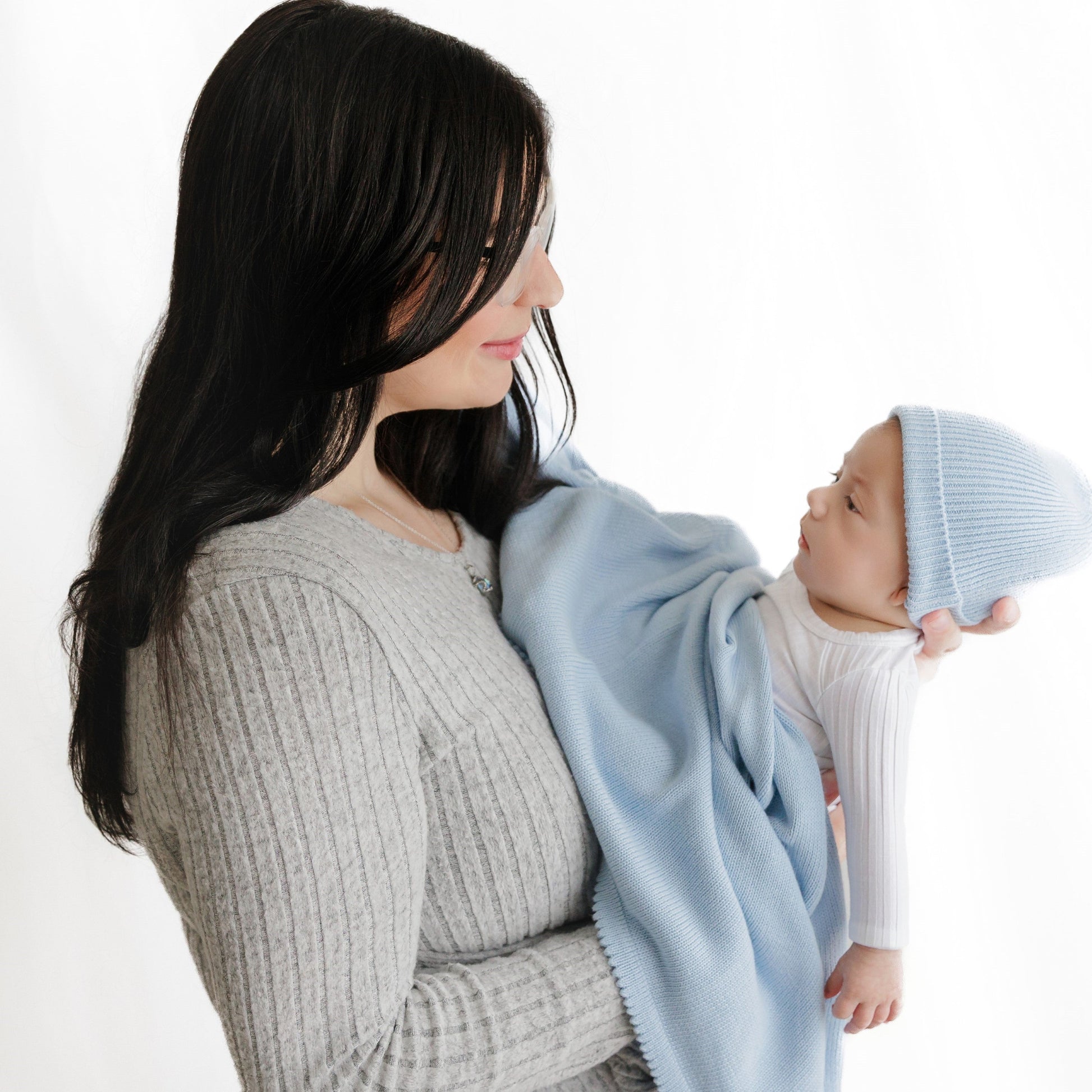 Woman holding a baby wrapped in a light blue blanket against a white background