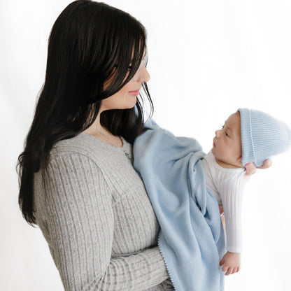 Woman holding a baby wrapped in a light blue blanket against a white background