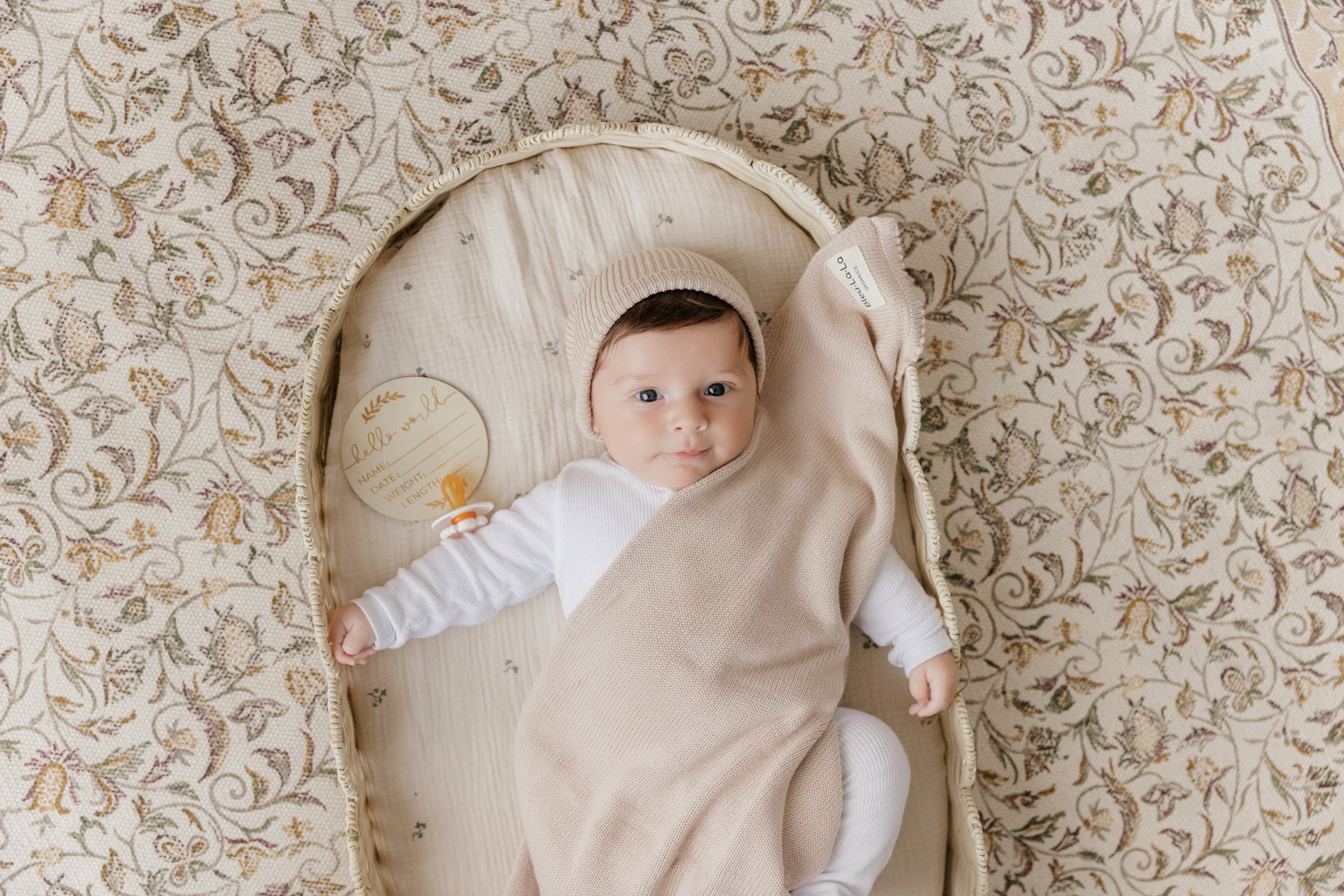 Baby wrapped in a beige swaddle blanket from Bleu-la-la, on a floral-patterned surface