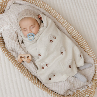 Newborn baby wrapped in a textured blanket with a pacifier, lying in a woven basket.