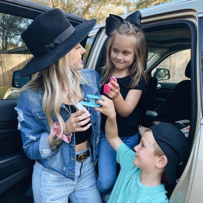 Woman with a large black hat interacting with two children in a car  all holding an Unbuckle Me in hands.