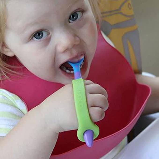 Child using a green and purple toothbrush with EaZyHold grips and a red bib.