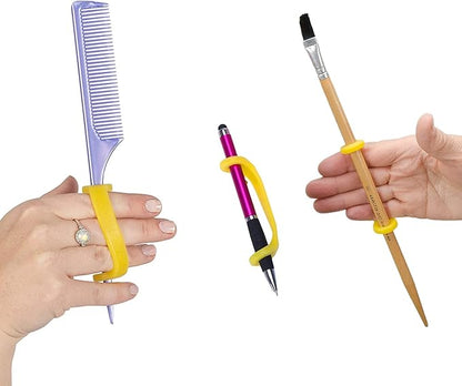 Hands holding a comb, pen, and paintbrush with yellow EazyHold grips on a white background