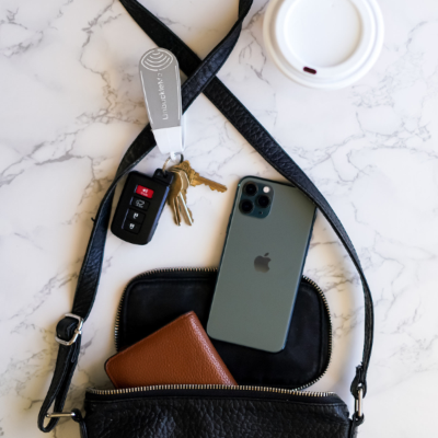 Black crossbody bag with phone, wallet, keys, and car key fob on a marble surface.