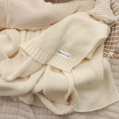 Cream-colored knit Blue-La-La blanket with a brand label on a textured surface
