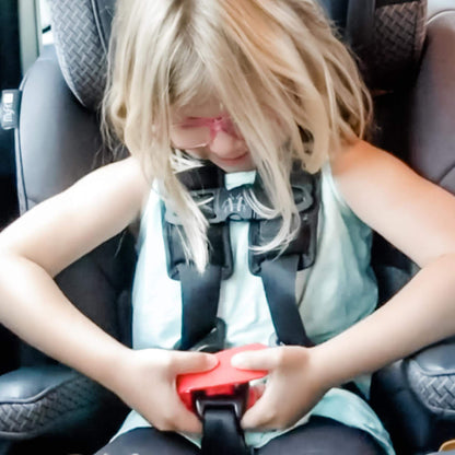 Child in a car seat being buckled up with a red UnBuckleMe tool using it on her car seat.