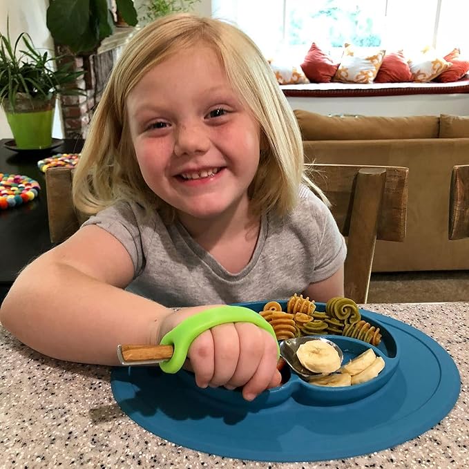 Child sitting at a table with a blue placemat, eating bananas and using a  spoon with EaZyHold grips.
