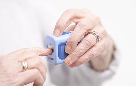 Light blue plastic electric nail clipper, dark blue textured grip, in use.