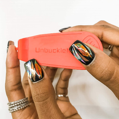 Person holding a red product labeled 'Unbuckled' with colorful nail art.