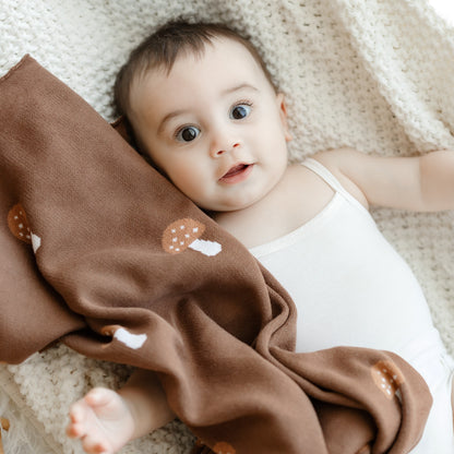 Baby lying on a soft surface with a brown blanket featuring mushroom patterns.