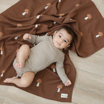 Baby lying on a brown blanket with mushroom patterns 