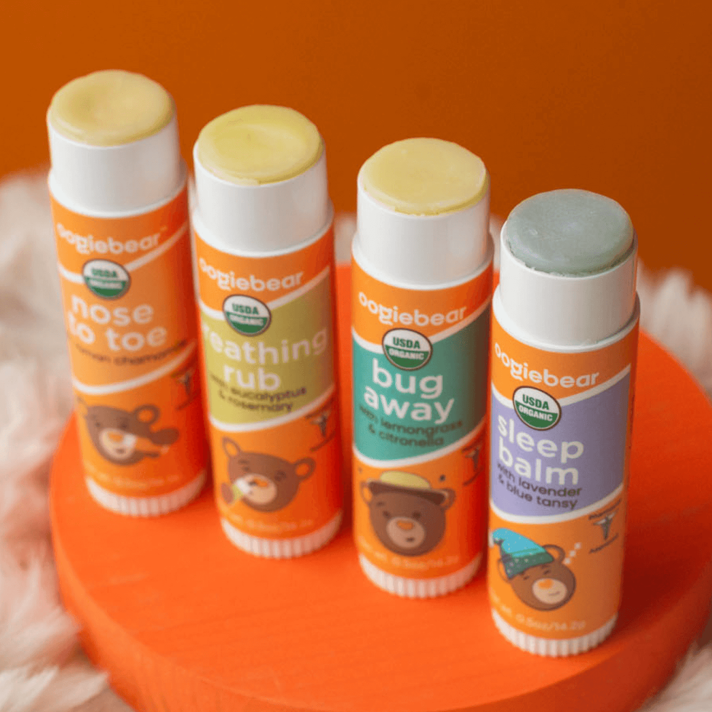 oogiebear 4-pack balm collection with Nose to Toe, Breathing Rub, Bug Away and Sleep Balm tubes with caps off.