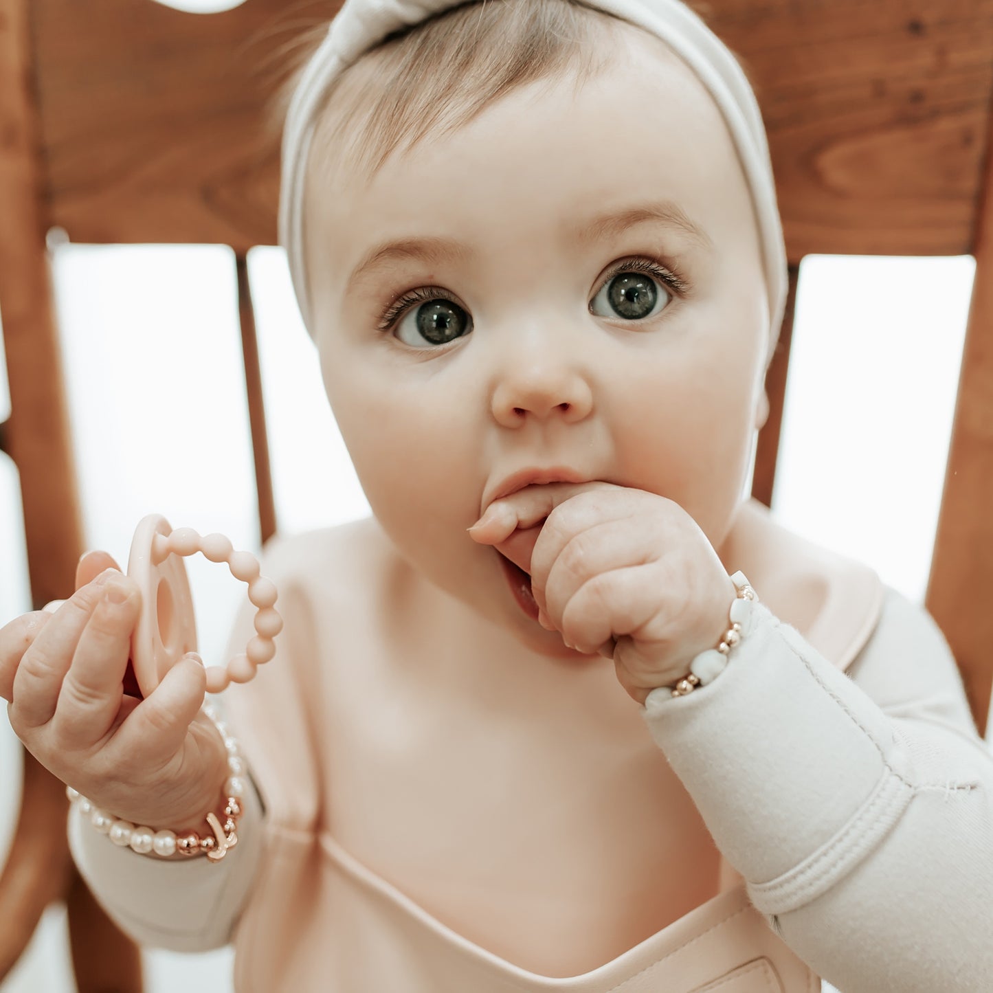 Baby wearing a white headband and holding a teething ring indoors.