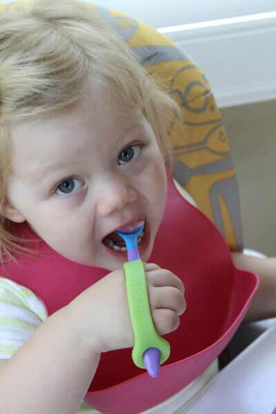 Child eating using EazyHold grip tool with spoon in a high chair.