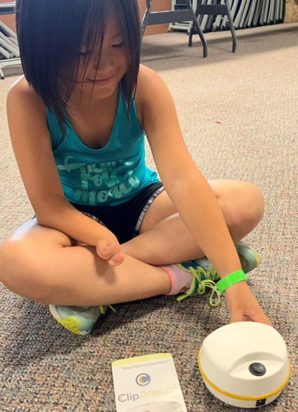 Child sitting on the floor with the use of only one hand. She is using the ClipDifferent Junior which is now the POD and Child size Lil Nipper.