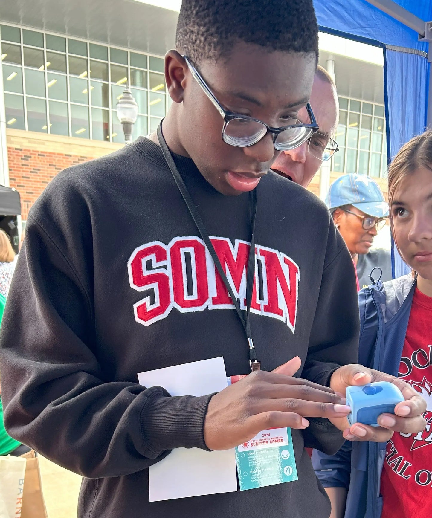 Young man wearing a 'SOMN' sweatshirt using the lil nipper to trim his nails. The Lil Nipper Adult (Blue) electric nail clipper, designed for safe and easy trimming of adult nails.
