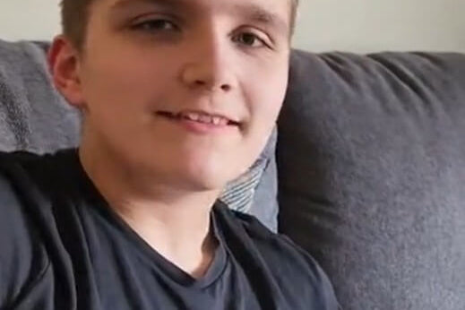 Person wearing a black Under Armour shirt sitting on a gray couch smiling with Lil Nipper in hand.