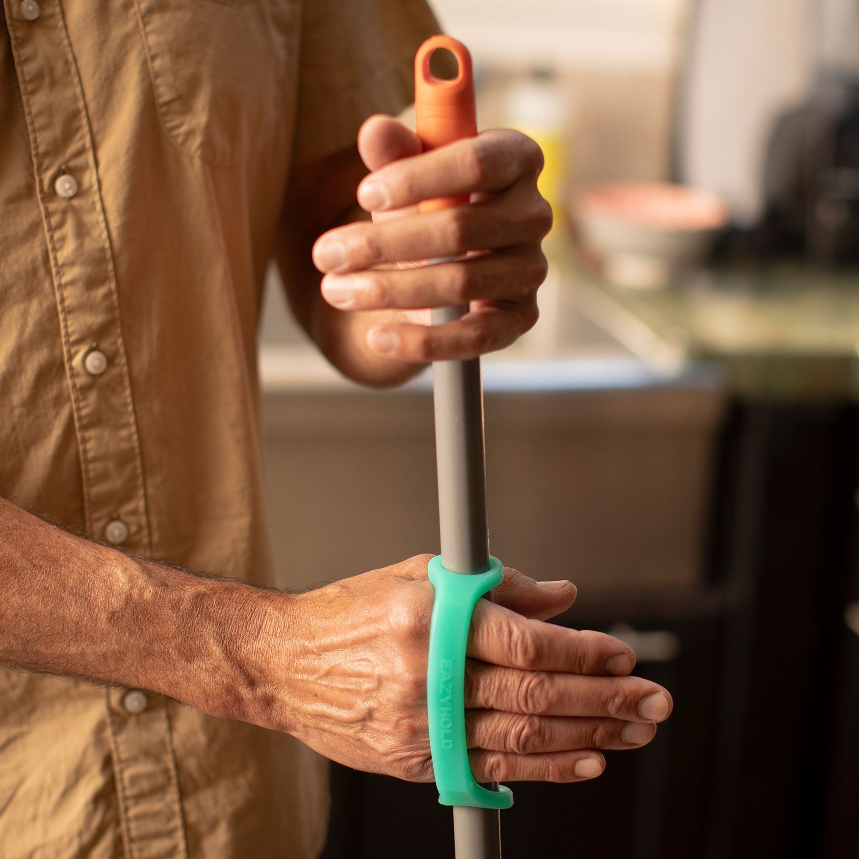 Person holding a cane and green grip handle in a blurred kitchen setting