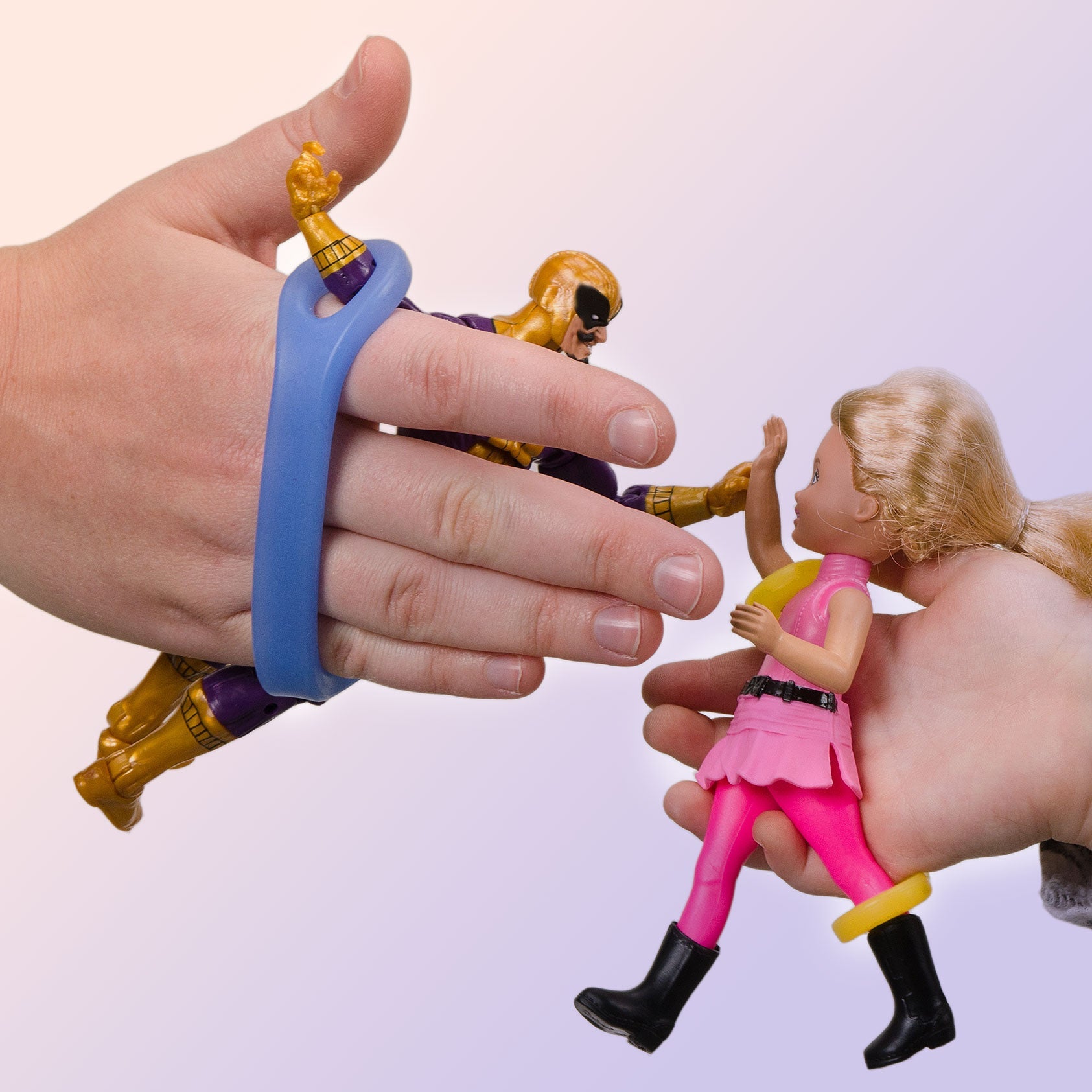 Hand holding a blue plastic gripping tool near action figures on a plain background