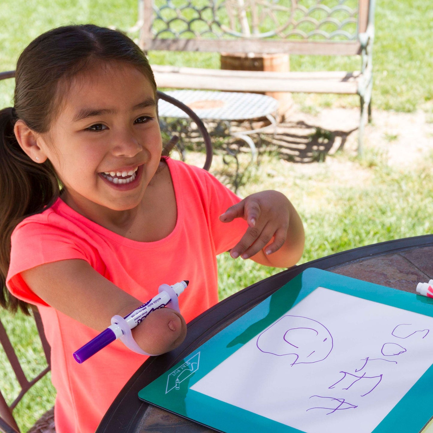 Young girl with one hand using grippy tool writing on a portable whiteboard outdoors.