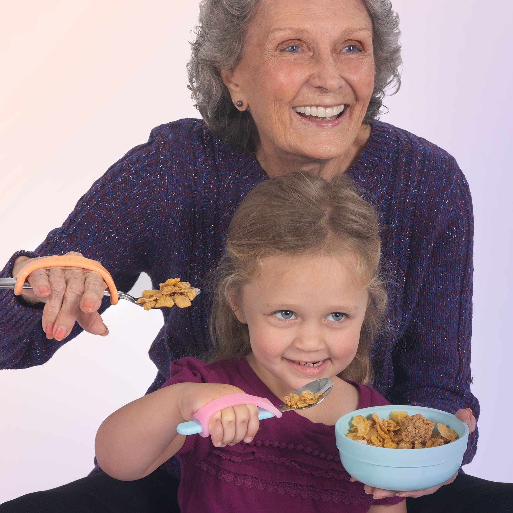 Grandmother and granddaughter eating cereal with spoons against a white background