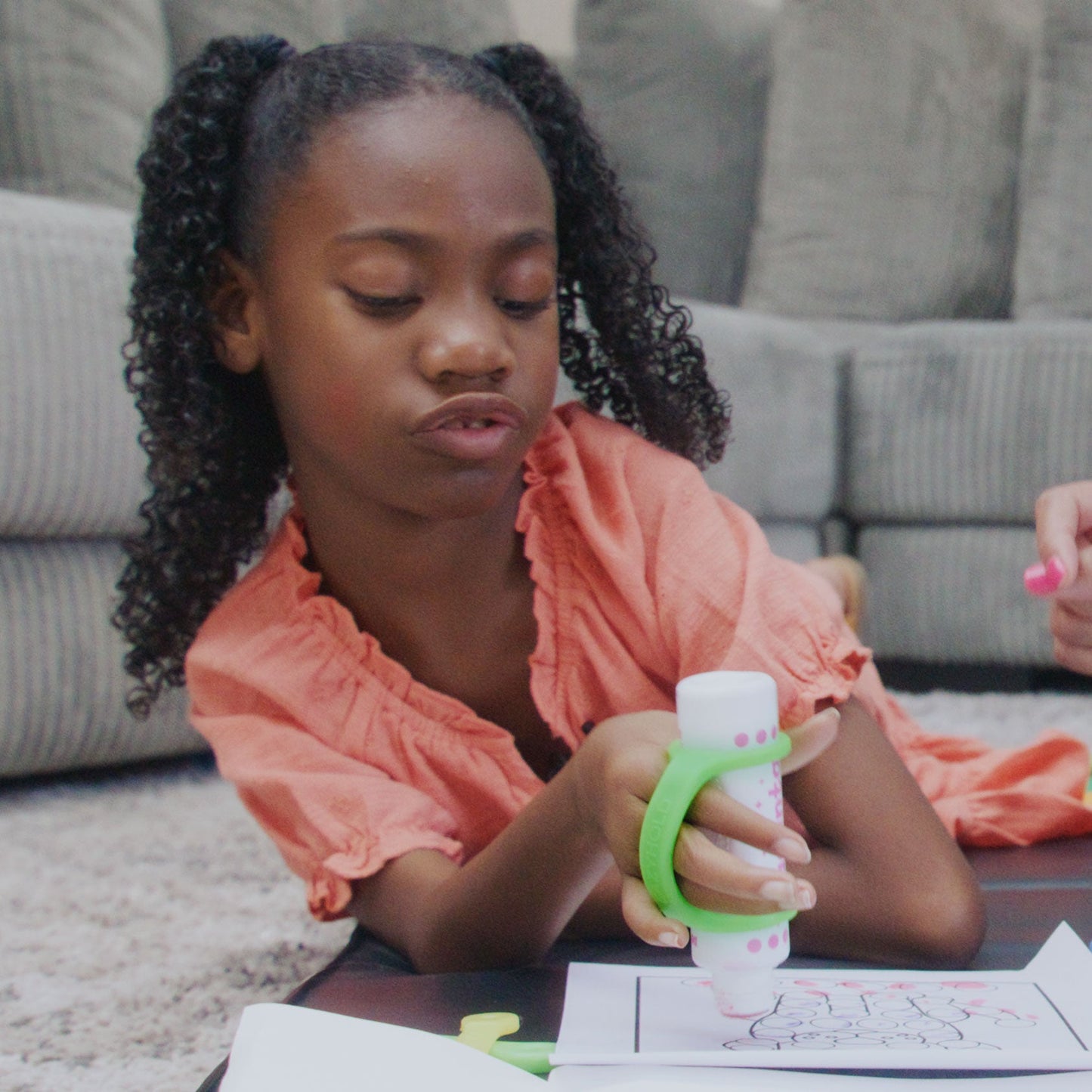 Young girl coloring using EazyHold grip tool with a dotter in a casual indoor setting.