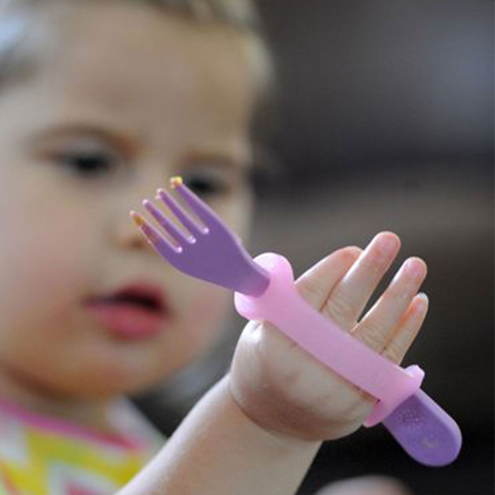 Child's hand with a purple and pink utensil trainer device