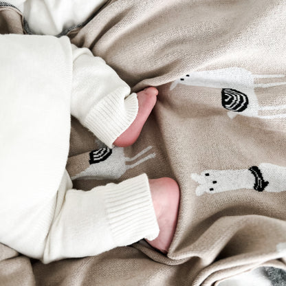 Close-up of a baby's feet in white socks with black and white lama patterns on beige fabric.