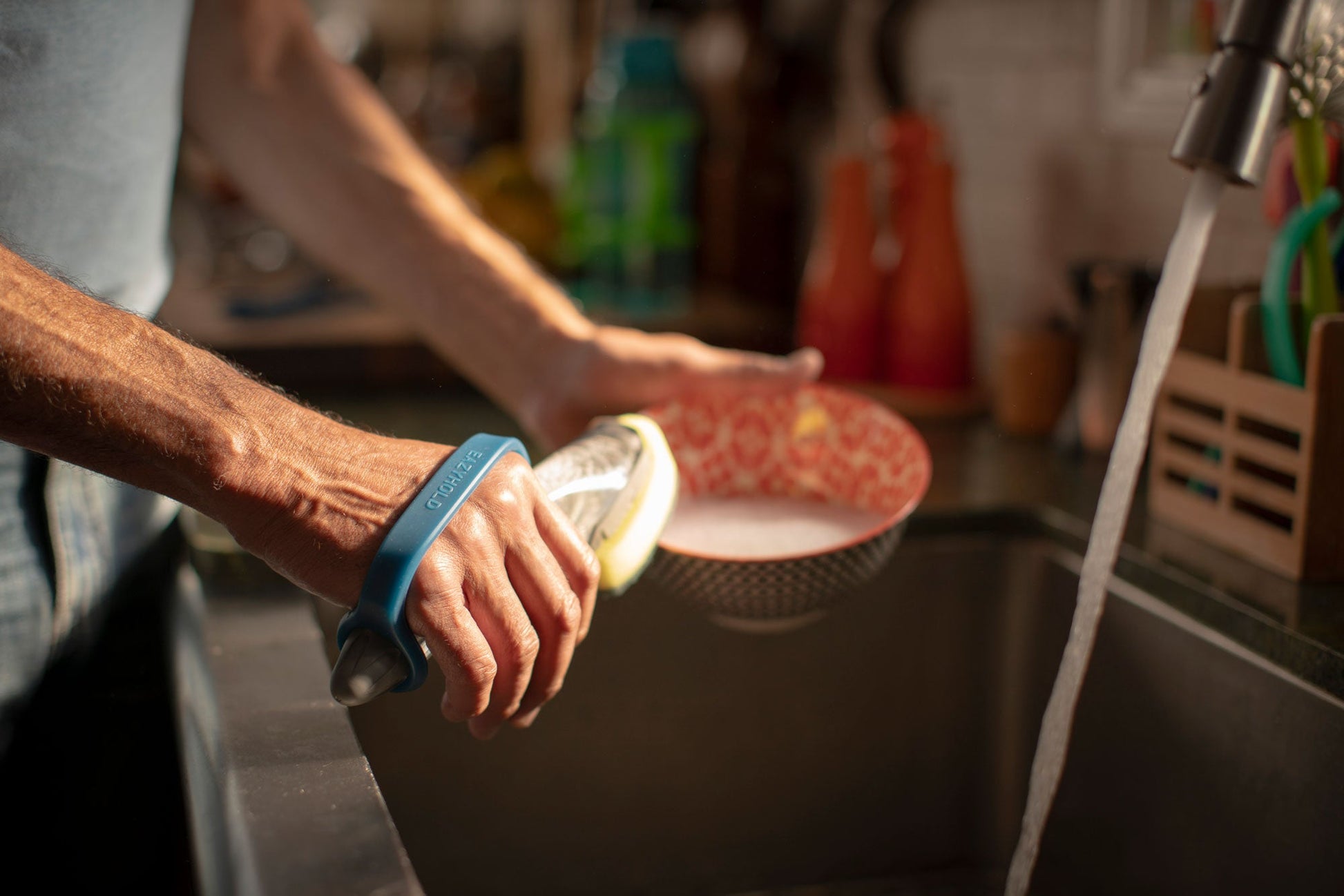 Senior woman washing dishes in a kitchen sink with a focus on the hand using EazyHold grips with sponge.