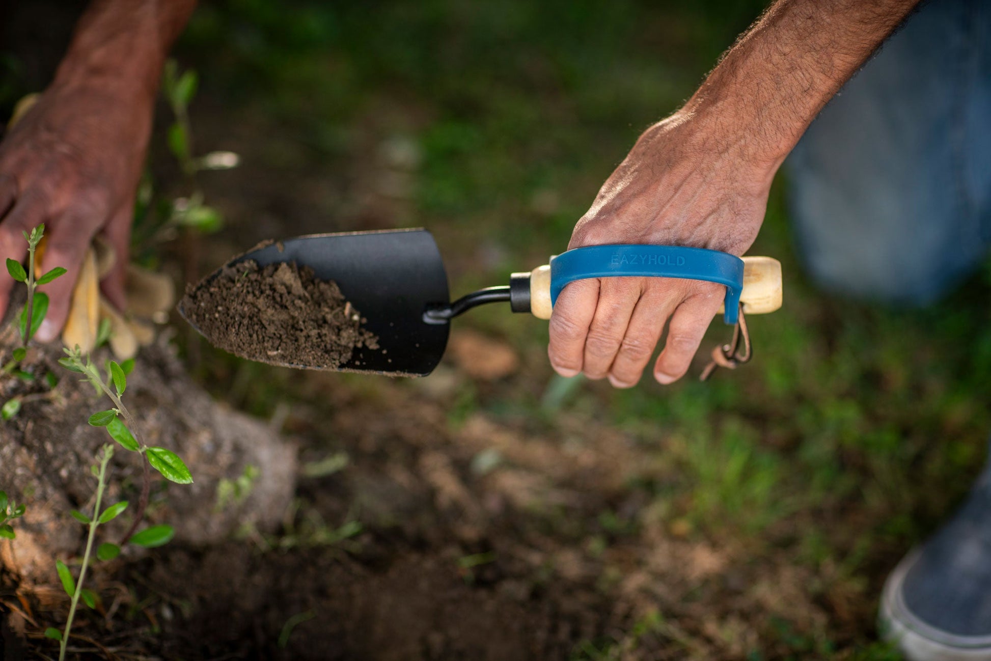 Person holding a trowel with EazyHold grips soil in a garden setting