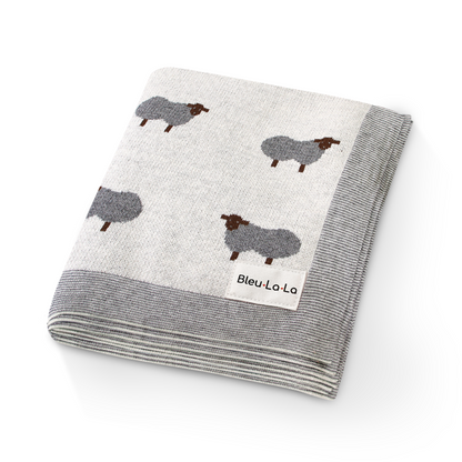 Folded blanket with sheep pattern and 'Bleu Lo La' label on a white background