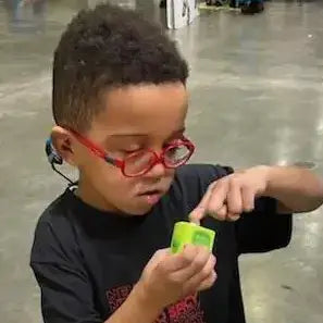 Young boy with red glasses using a Lil Nipper and he is inserting his fingernail. He has Autism and is around 7 years old.
